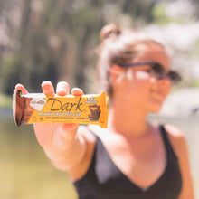 Load image into Gallery viewer, Woman outside with sunglasses on holding out a Peanut Butter Cup bar
